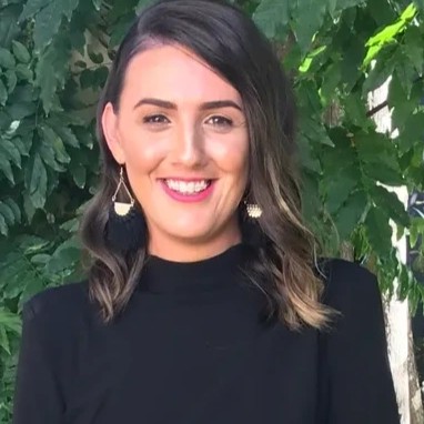 Georgie Charles, smiling, in front of green leaves